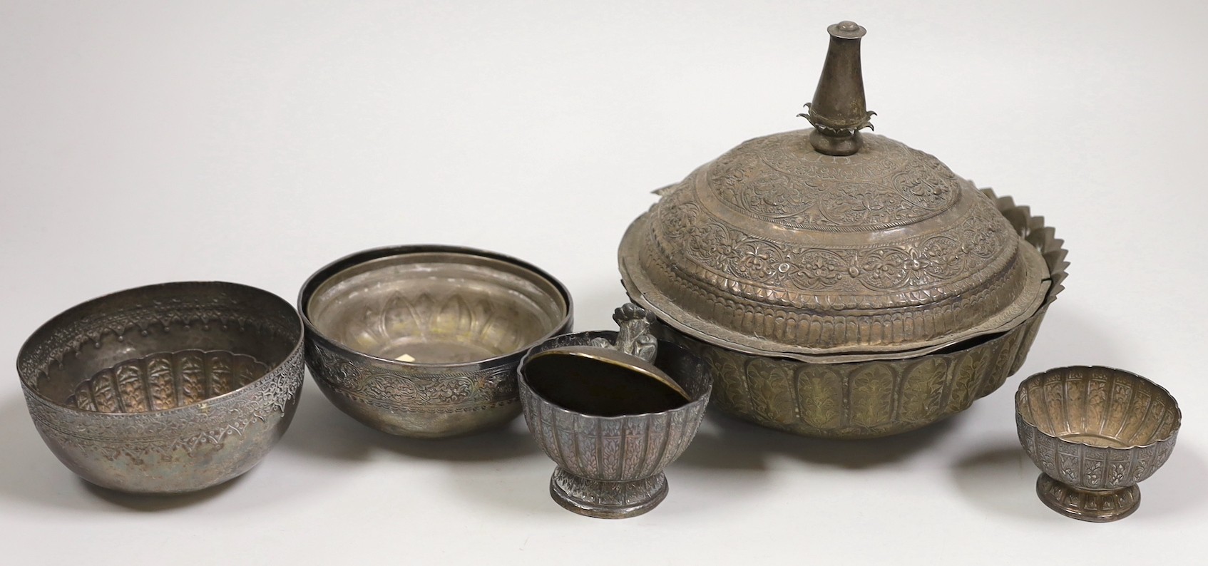 A Malay Straits pedestal bowl and cover or 'Batil Ber Tutop' (a.f.), three Malay Straits white metal betel nut cups and two similar small bowls, all with embossed floral or foliate designs (one cup with green enamelled d